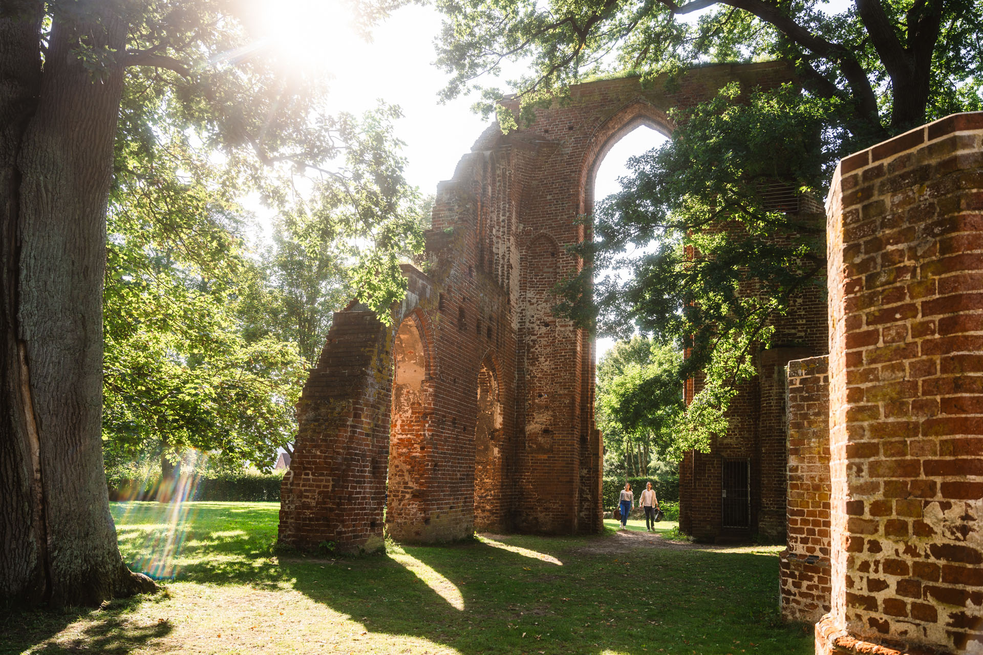 The Eldena monastery ruins against the sun. There are two people under the large arc.